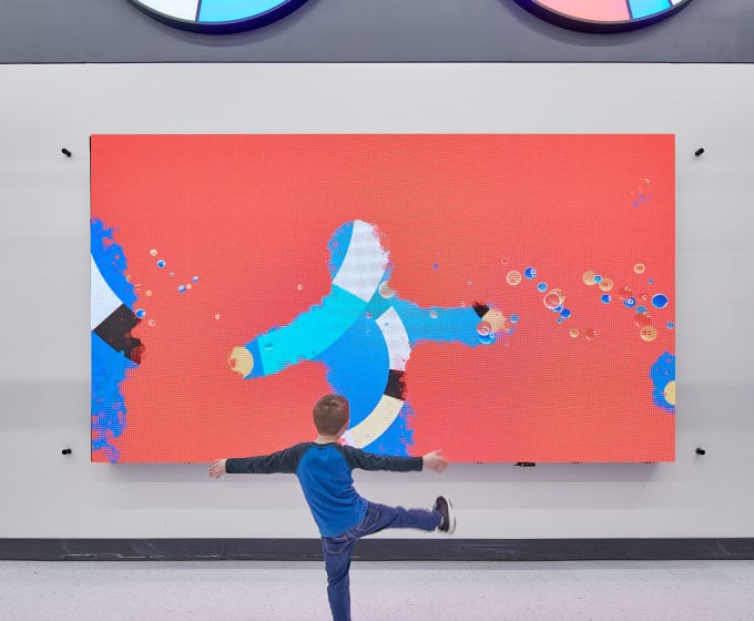 A kid lifts his feet high up in front of the AI interactive wall. Image via Walmart